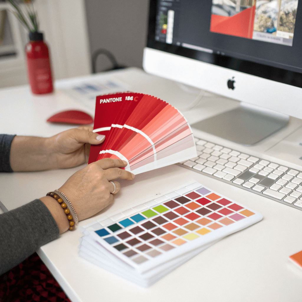 Designer checks printed box color accuracy against Pantone Solid Coated fan deck swatch.